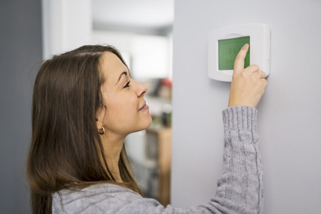 Woman set the thermostat at a house.