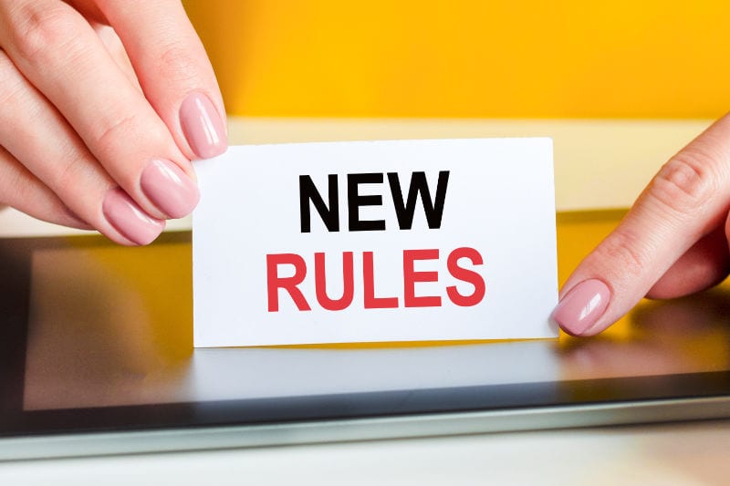 woman's hands holds a piece of white paper with the text: new rules. Yellow background, surface of the tablet screen, close-up. Can be used for business, marketing, financial concept, AC.